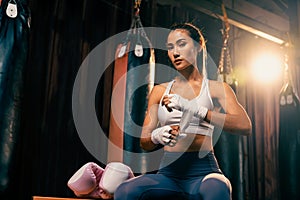 Determined Asian female Muay Thai boxer wraps her hand. Impetus