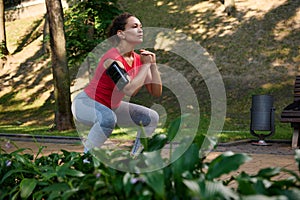 Determined athlete, sportswoman exercising outdoor, doing deep squats in the city park. Sport, fitness, functional body weight