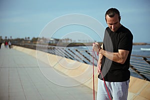 Determined athletic man with performing bodyweight training, using a resistance fitness band, doing exercises on biceps