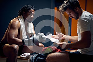 Determined boxing player with serious face in sweats after workout resting with his coach, getting consultation