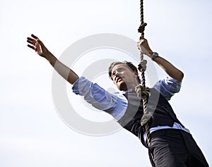 Determined businessman climbing a rope, reaching