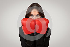 Determined businesswoman with a focused gaze wearing boxing gloves, symbolizing empowerment