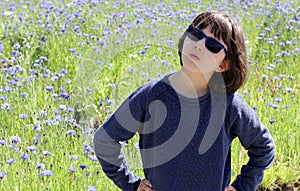 Determined child with blue sunglasses over beautiful floral meadow, outdoor