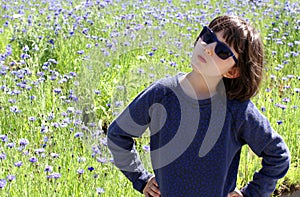 Determined child with blue sunglasses standing over beautiful floral field
