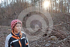 Determined facial expression or expression at the moment of an idea. Piles of branches on the ground, sunset behind the bare trunk