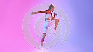 Determined Fitness Lady Jumping Exercising Holding Dumbbells Over Neon Background