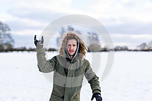 A determined looking young man with a snowball in hand ready to throw it during a snowball fight. He is in a snow covered wintery