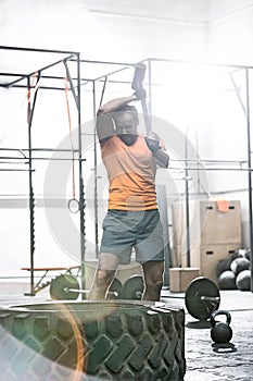 Determined man hitting tire with sledgehammer in crossfit gym