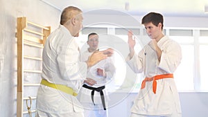 Determined motivated senior man wearing kimono working on hand strikes and martial arts skills in sparring with young
