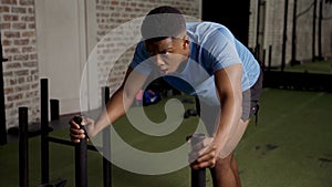 Determined muscular young black man doing sled push workout at the gym