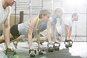 Determined people doing pushups with kettlebells at crossfit gym