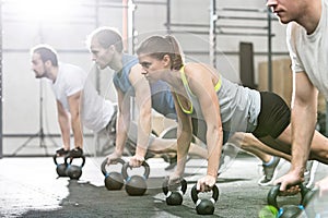 Determined people doing pushups with kettlebells at crossfit gym