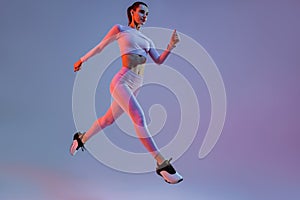 Determined sporty woman running in Mid-Air exercising during cardio workout over studio background