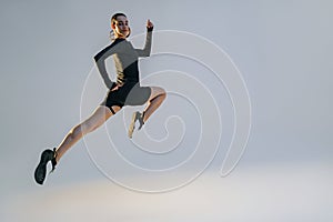 Determined sporty woman running in Mid-Air exercising during cardio workout over studio background