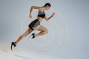 Determined sporty woman running in Mid-Air exercising during cardio workout over studio background