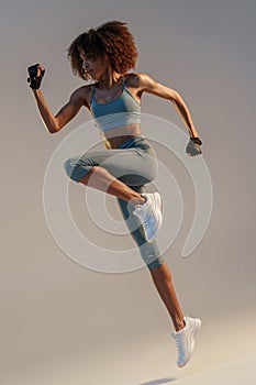 Determined sporty woman running in Mid-Air exercising during cardio workout over studio background