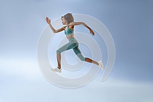 Determined sporty woman running in Mid-Air exercising during cardio workout over studio background