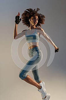 Determined sporty woman running in Mid-Air exercising during cardio workout over studio background