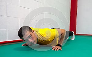 Determined strong young man doing push-ups and looking at camera.