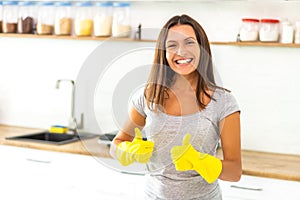 Determined wife in yellow gloves is ready and eager to start cleaning her modern kitchen and gives thumbs up.