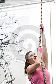 Determined woman climbing rope in crossfit gym