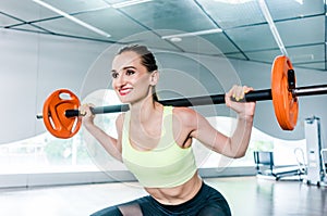 Determined woman holding a barbell behind the neck during functional training workout