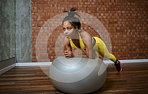 Determined young African American woman doing plank on a fitness ball at gym studio