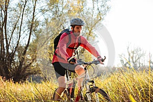 Determined young bearded mountain biker riding along a path through tall grass