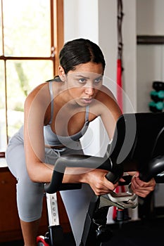 Determined young biracial woman doing cardio workout on exercise bike at the gym