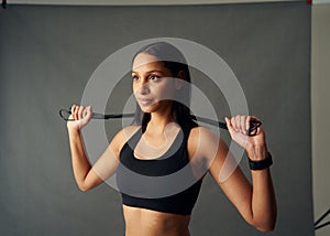Determined young biracial woman in sports bra holding jump rope behind neck in studio