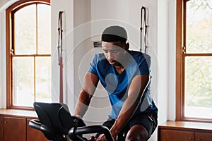 Determined young black man doing cardio workout on exercise bike at the gym