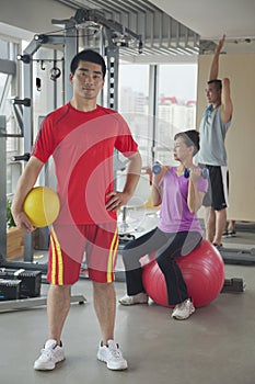 Determined young man holding ball in the gym, people working out in the background