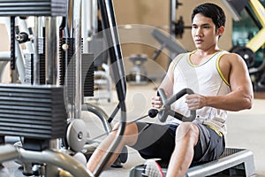 Determined young man looking forward while rowing at the cable machine