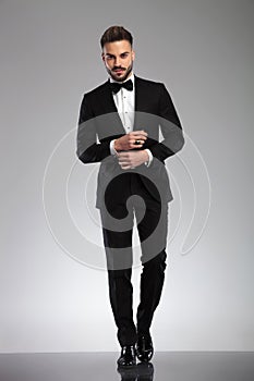 Determined young model adjusting his cuff while wearing tuxedo