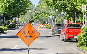 Detour Sign pointing in two directions with a tree filled Street with barricades.