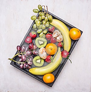 Detox and diet food concept, fresh fruit, bananas, grapes, kiwi and tangerine, strawberry lined vintage wooden box top view