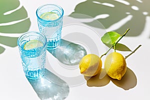 Detox lemon water in blue glasses with fresh lemons, sunlight and shadows