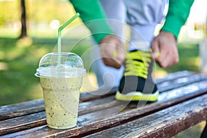 Detox smoothie drink and running footwear close up. Man athlete tying sport shoes.