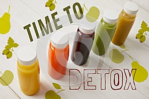 detox smoothies in bottles standing in row on white wooden background, time to detox inscription