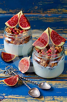 Detox superfoods breakfast or healthy dessert - chia milk pudding with granola and fresh figs in the glass jars on the blue table