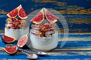 Detox superfoods breakfast or healthy dessert - yogurt with granola and fresh figs in the glass jars on the blue wooden background