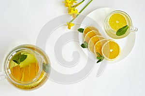 Detox tea in transparent teapot with orange fruit and mint and yellow Narcissus flower on white background. Spa and relaxation