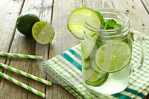 Detox water with lime and cucumbers in jar against wood