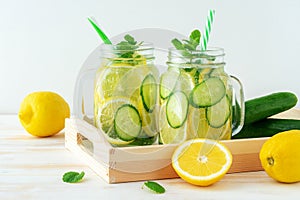 Detox water with sliced lemon and cucumber in a jar on wooden table. Healthy concept