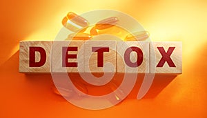 Detox word made with wooden blocks and oil capsuless around on orange background. Medical healthcare concept