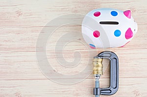 Piggy bank and coins squeezed tightly in a G-Clamp over wooden background