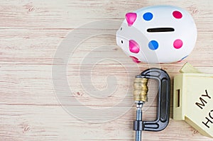 Piggy bank and coins squeezed tightly in a G-Clamp over wooden background