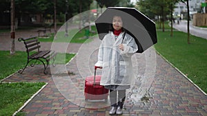 Devastated depressed little woman crying standing on city street with umbrella and travel bag. Wide shot portrait of