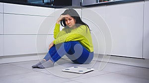 Devastated dieting young asian woman sitting on the flor with weight scale in front. Weight loss and mental health