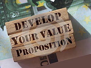 Develop your value proposition on wooden building blocks standing on 100 Euro bills. Business marketing concept